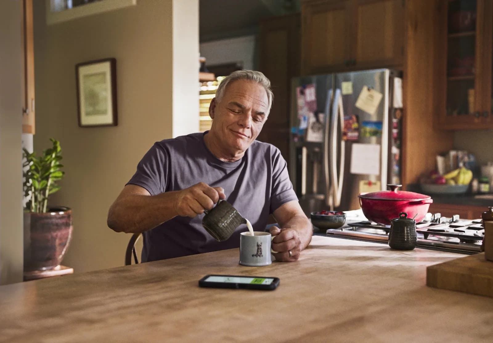 A man at his kitchen counter with his glucose readings on his phone beside him